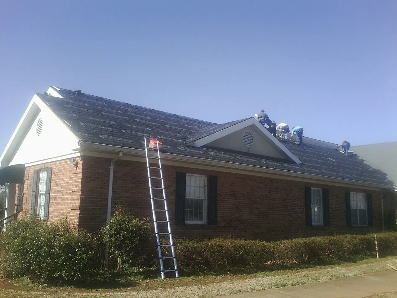 Crew tearing shingles off a brick ranch roof with a ladder set — Emergency Roof Repair work by our crew in Krotz Springs