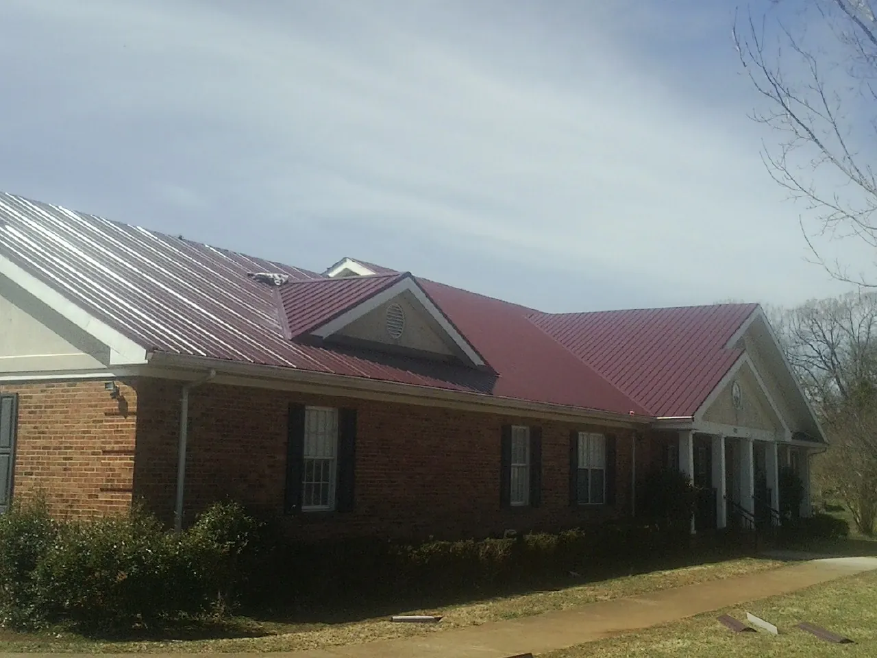 Red metal roof with gabled entries on a long brick building, from a Hail Damage Roof Repair job in Krotz Springs