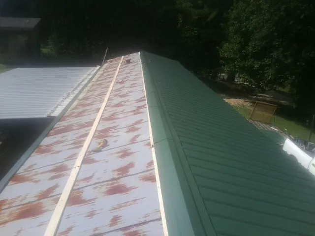 Old rusted panels beside newly installed green metal roofing — Wind Damage Roof Repair by Roofing Brothers in Krotz Springs