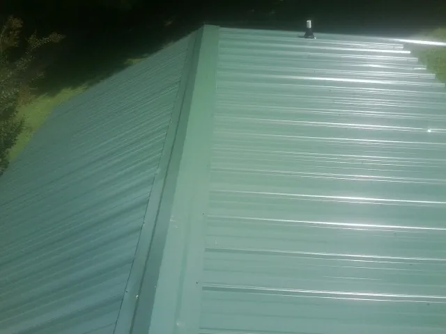New green metal panels meeting at the ridge of a roof — Flat Roof Repair work by our crew in Krotz Springs