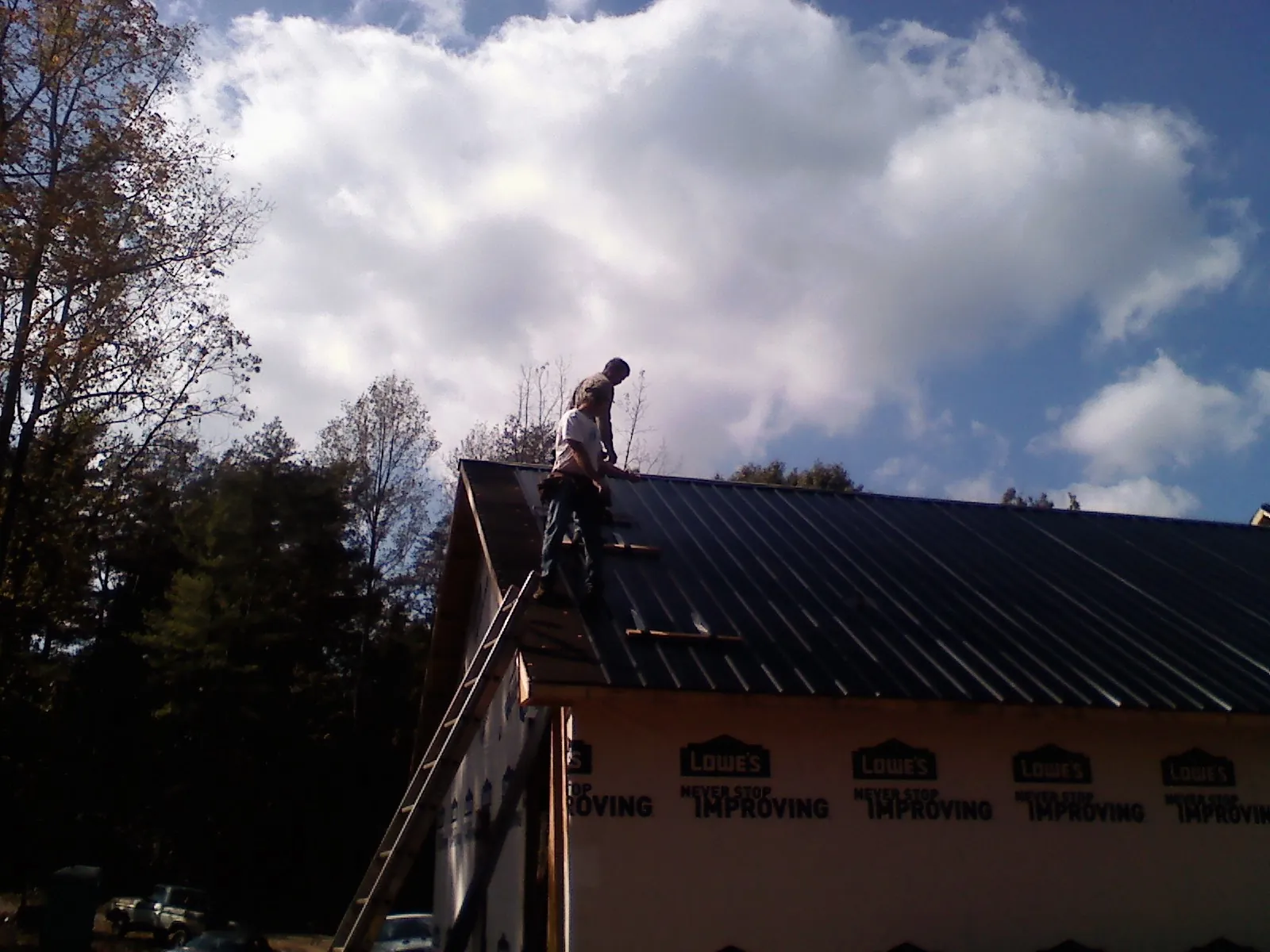 Roofer fastening dark metal panels high against a cloudy sky, from a Roof Inspection job in Krotz Springs