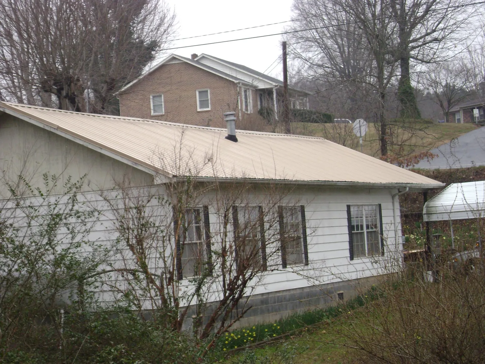 Tan metal roof on a white sided house set into a hillside — Commercial Roofing by Roofing Brothers in Krotz Springs